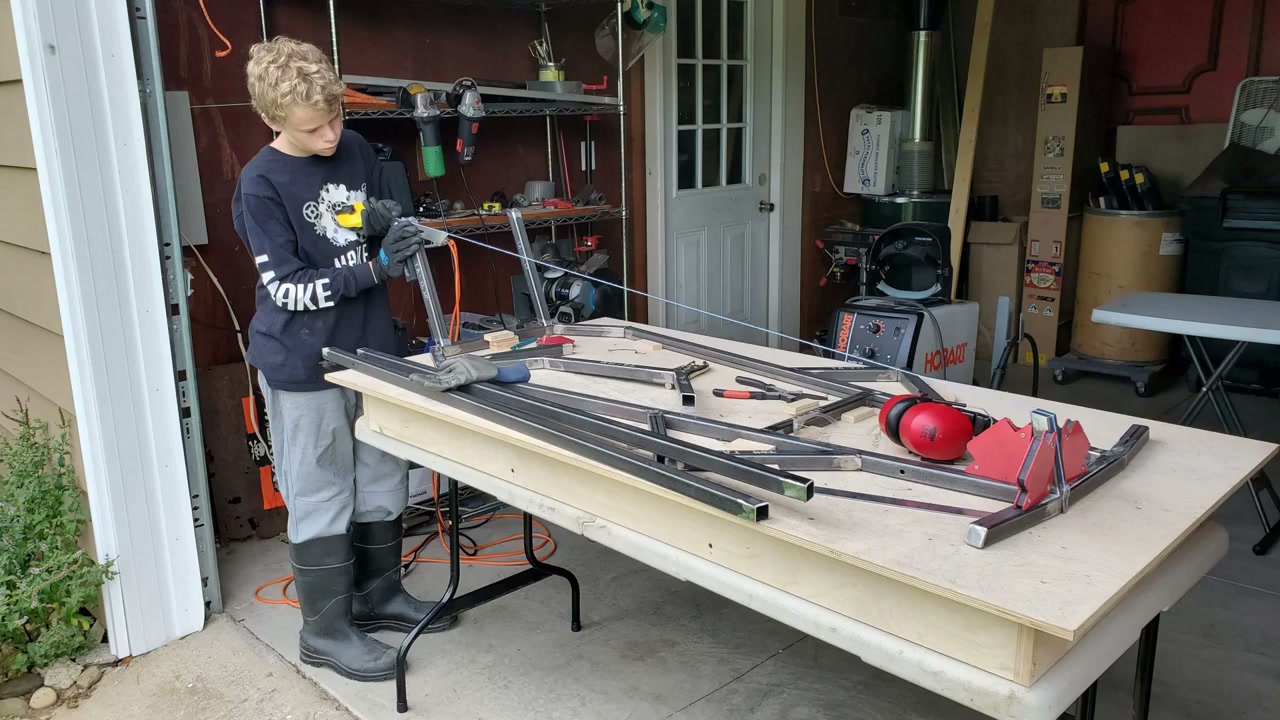 Young builder cutting steel tubing on a garage work table with a Hobart welder nearby