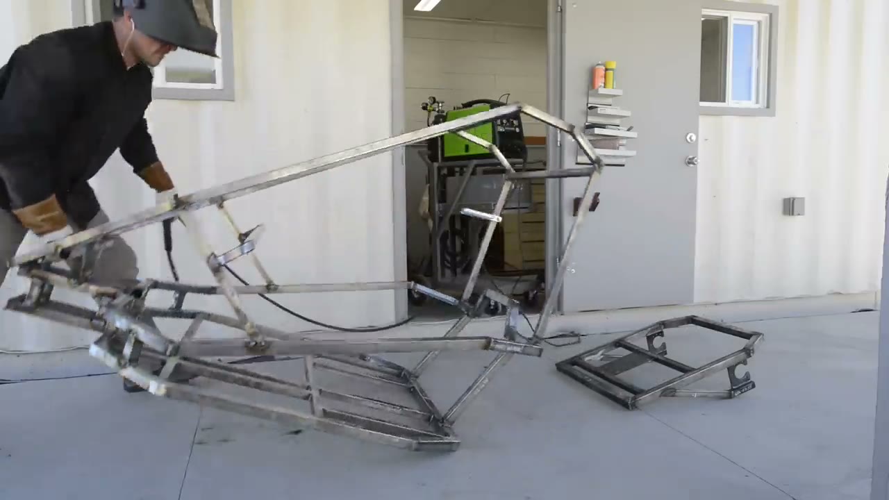 Builder lifting the welded go kart frame outside a workshop